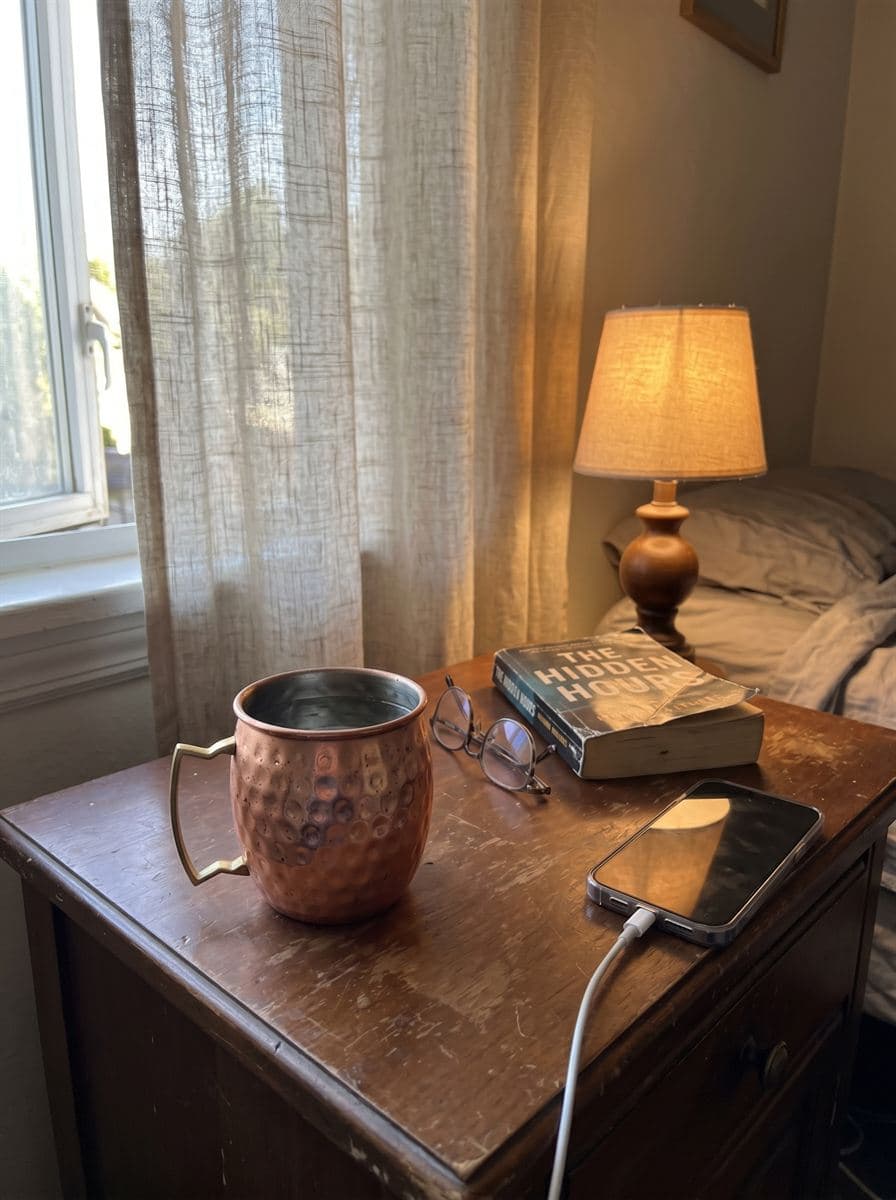 A copper cup of water on a bedside table in soft morning light