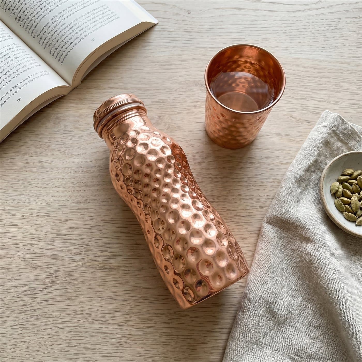 An overhead flat-lay of the curved copper bottle and tumbler on a pale table