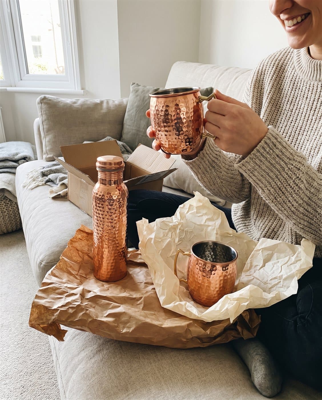 Unwrapping the copper ritual set — bottle and two mule mugs — on the sofa at home