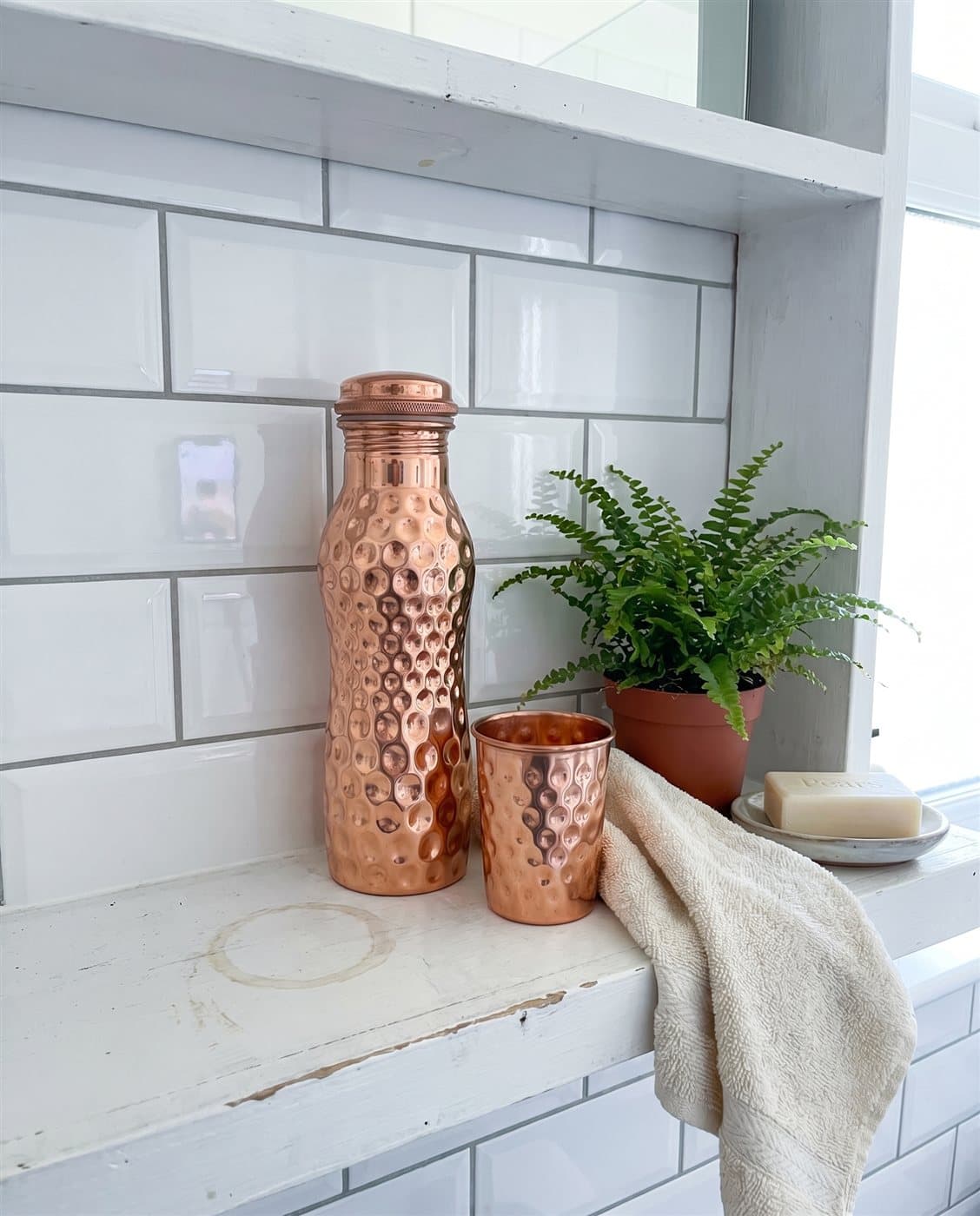 The curved copper bottle and a copper tumbler on a bright bathroom shelf